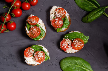 Homemade sandwiches with curd cheese, tomatoes, spinach on a Greek roll without yeast on a dark background, copy space