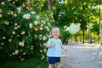 Adorable little girl with green balloon outdoors in park on a sunny day