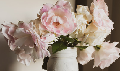 Full frame closeup of wilting pink and cream roses in jar with vintage filter effect and moody...