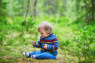 Adorable baby girl in the forest, sitting on the ground and playing with pine cones