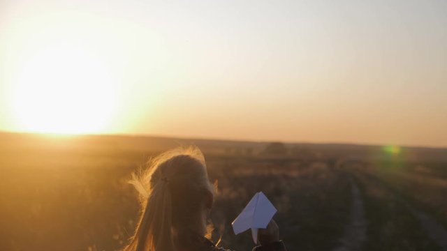 Happy little girl playing with a paper airplane outdoors during sunset. Concept big child dream.