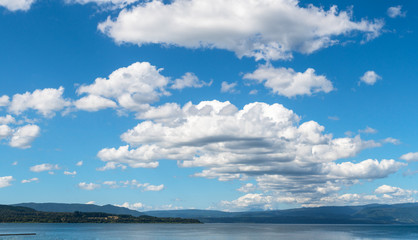 Naklejka na ściany i meble Panoramic photo of a group of white clouds between a blue sky and a lake in southern Chile
