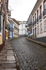 Fototapeta premium Vertical steep wet cobblestone street leading to white corner building passing the typical historic colonial colourful exterior facade architecture