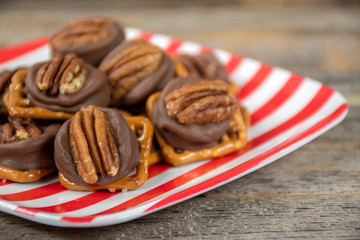 close up of pecan nut and melted chocolate on salty pretzel on red and white striped plate