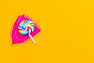 Lollipop lies on a feather. spiral candy on a yellow background. holiday decoration