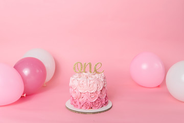 Pink studio backdrop with first birthday cake with shades of pink rosettes made from frosting with an ombre theme and balloons