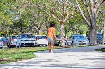 indian cuban boy, run holding, long board, action turn away, park sidewalk, orange shirt glasses, brown hair tanned skin