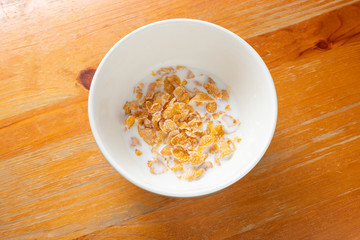 Bowl of cornflakes in milk on wood background from above.
