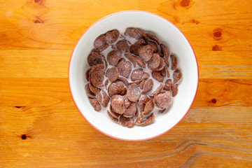 Chocolate cereal in a bowl on a wooden floor from above.