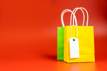 Yellow and green gift or shopping bags with blank tag isolated on red background