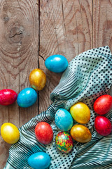 Colorful Easter eggs and silk textile material on the wooden background. Festive Easter holiday concept. View from above. Copy space. Top view