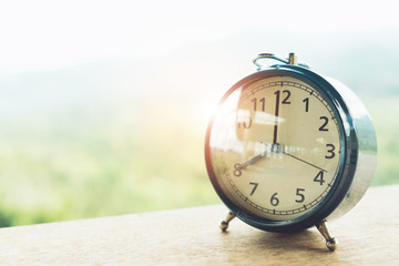 Selective focus of alarm clock on table with nature bokeh mountain background.