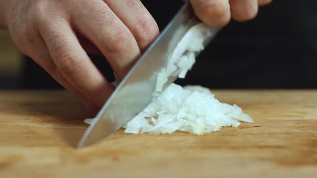 Close-up of man hands cutting white onions on a wooden chopping board with a kitchen knife. Stock footage. Preparing food.