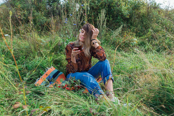 Fototapeta premium Beautiful woman with camomile flower in hair sitting on the grass and drinking tea outdoors