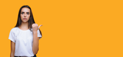 Beautiful caucasian woman shocked by something is pointing to the yellow blank space near her
