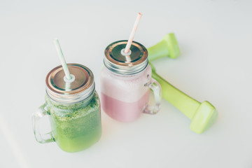 Healthy smoothie options in eco friendly glass jars with paper straws and light dumbbels in a luxury gym recreation area or vegan cafe. Trendy muted toning, place for text