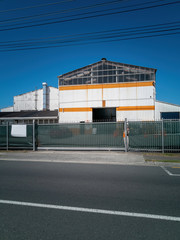View of typical retail and packing warehouse painted in white and yellow behind fence in industrial suburb