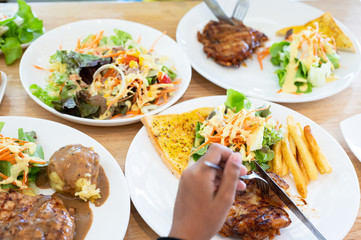 Close up knife and fork cutting grilled chicken steak set in white dish on wooden table background.Chicken grill, mashed potato, bread and salad.Restaurant menu.