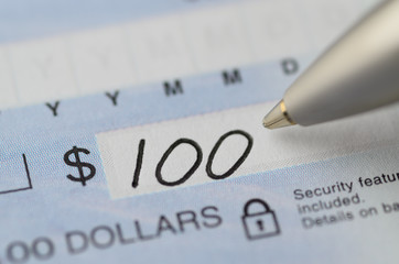 Close up of pen writing the dollar amount begining with 100 on a cheque with security features