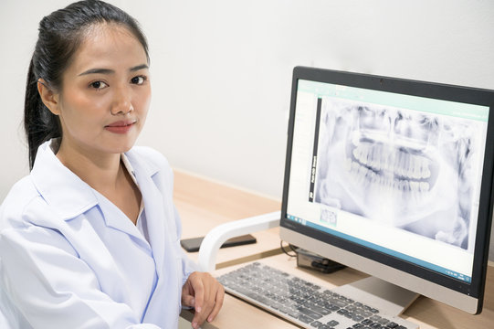 Portrait Asian woman dentist sitting and looking tooth image x-ray in computer.Female doctor examining patient tooth with panoramic radiograph on dental chair at the dental office.