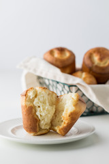 A close up of a baked popover on a plate with a basket of popovers in behind.