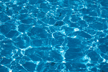 Blue and bright ripple water surface in swimming pool with sun reflection.