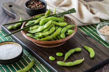 A rustic bowl filled with edamame beans and chopsticks ready for eating.