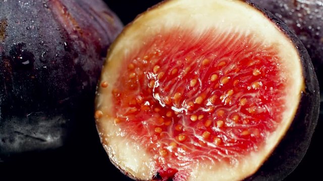 Closeup 4k video of water droplets falling on fresh ripe fig cut in half. Perfect abstract shot for organic food and healthy nutrition. Closeup of fruits
