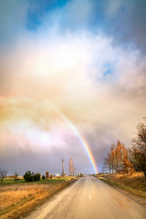 Naklejka na ściany i meble Early spring landscape with dramatic sky, rainbow and road lines