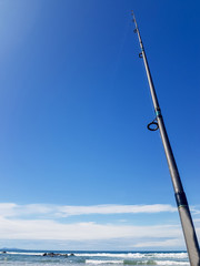 Fishing rod rising into blue sky on summer day.