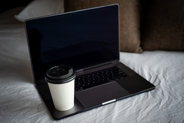 Coffee Cup To Go, Laptop and smartphone on bed. Working from home concept. Green template on screen.