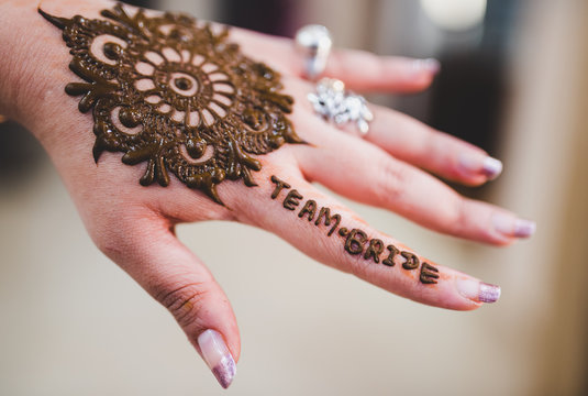 Close up of 'Team Bride' written on a girl's hand with Mehendi tattoo artwork. Mandala pattern green Henna art on a bridesmaid hand at a Mehndi ceremony. Isolated hand with blurred background.