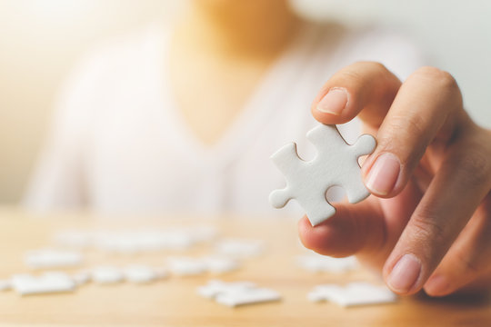 Hand of male trying to connect pieces of white jigsaw puzzle on wooden table. Healthcare for alzheimer disease, dementia, memory loss, autism awareness and mental health concept