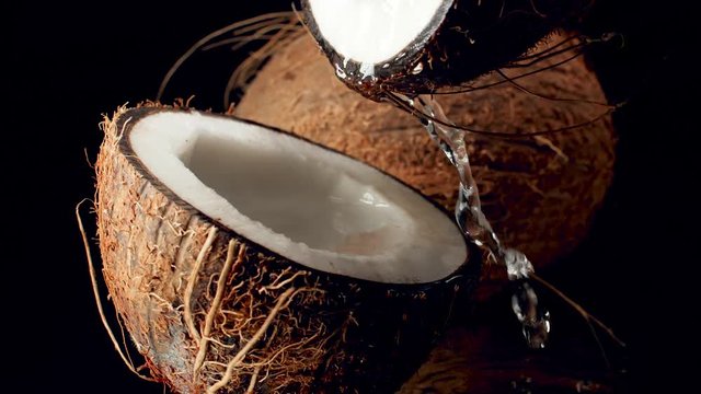 Closeup slow motion video of coconut milk slowly flowing out of broken coconut against black background. Perfect abstract backdrop for organic food and healthy nutrition.