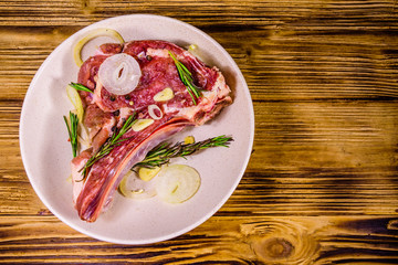 Raw ribeye steak, spices, rosemary, onion and garlic in a ceramic plate on wooden table. Top view