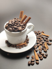 Cup full of coffee beans and cinnamon on a black background.