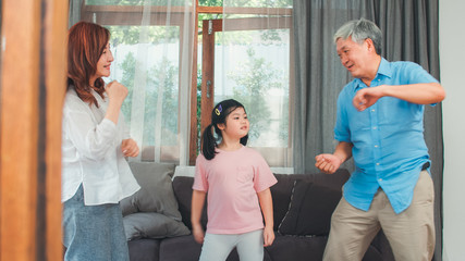 Asian grandparents and granddaughter listen to music and dance together at home. Senior Chinese, grandpa and grandma happy spend family time relax with young girl in living room concept.