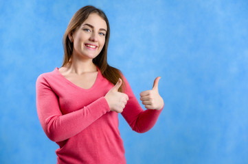 Fototapeta premium Portrait on a blue background of a pretty brunette Caucasian woman in a red sweater showing hands with a smile