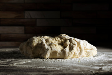 Fresh raw dough for making bread, pasta or pizza on a dark wooden table on a black background. Copy space