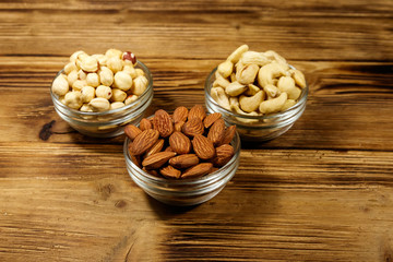 Assortment of nuts on wooden table. Almond, hazelnut and cashew in glass bowls. Healthy eating concept