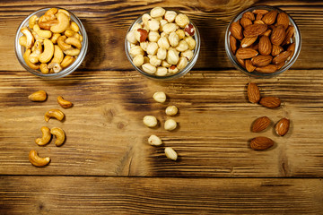 Assortment of nuts on wooden table. Almond, hazelnut and cashew in glass bowls. Top view. Healthy eating concept