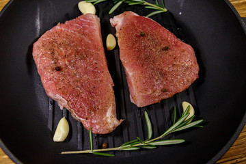 Raw pork steaks ready for preparation with rosemary, garlic and spices in cast iron grill frying pan