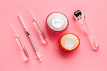 Dermatologist work desk with tools. Dermaroller, syringe, ampoule on pink background top-down flat...