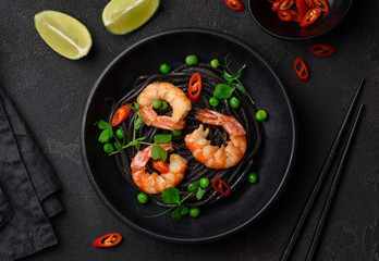 Black spaghetti. Cuttlefish ink pasta with shrimp, green peas and chilli in a black plate. Seafood noodles. Selective focus. Top view