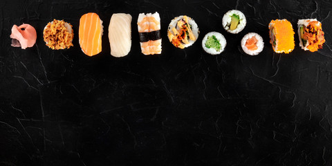 Sushi set, panoramic shot from above on a black background. Many different maki, nigiri and rolls, with fish and vegetables, with copy space