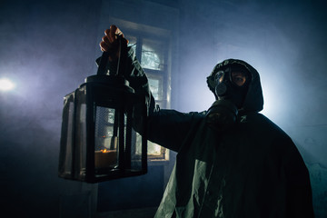 Dramatic portrait of a female wearing a gas mask in a ruined building with candle light and colorful smoke. 