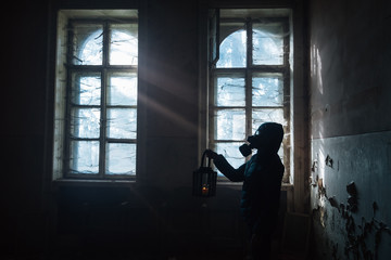 Fototapeta na wymiar Dramatic portrait of a female wearing a gas mask at a window with sun rays symbolizing Hope in a ruined building.
