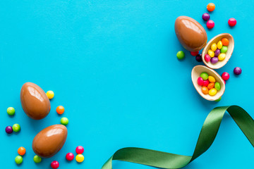 Easter background with chocolate eggs and dragees on blue background top-down frame copy space