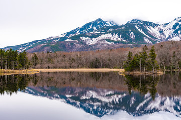 Small islet in the lake, beautiful lake surface reflecting blue sky like a mirror, rolling mountain range and woodland in the background on springtime sunny day. High latitude country natural scenery