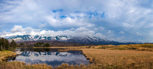 Beautiful lake reflecting blue sky like a mirror, rolling mountain range and woodland in the background on springtime sunny day. High latitude country natural beauty scenery